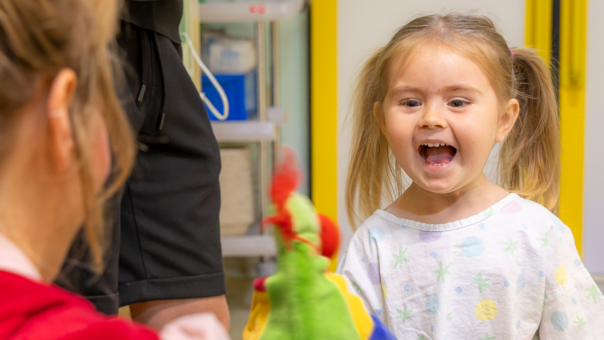 Ein kleines Mädchen, das lacht mit Clownin Lilo und ihrer Handpuppe.