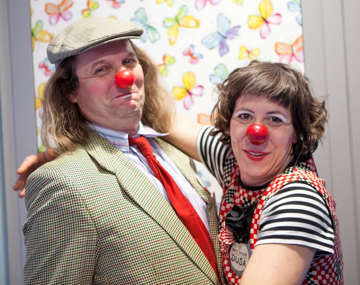 Clownin umarmt Clown, beide blicken in die Kamera