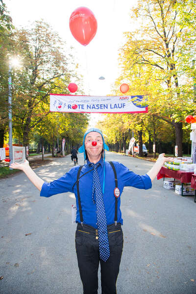 Ein Clown steht vorm Banner des ROTE NASEN LAUFS und ein Balloon schwebt über seinem Kopf