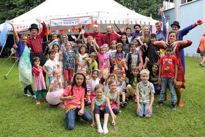 Gruppe an Kindern und Clowns posieren vor dem Zirkuszelt für ein Gruppenfoto