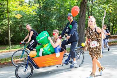 Clown schiebt verkleideten Läufer im Lastenfahrrad