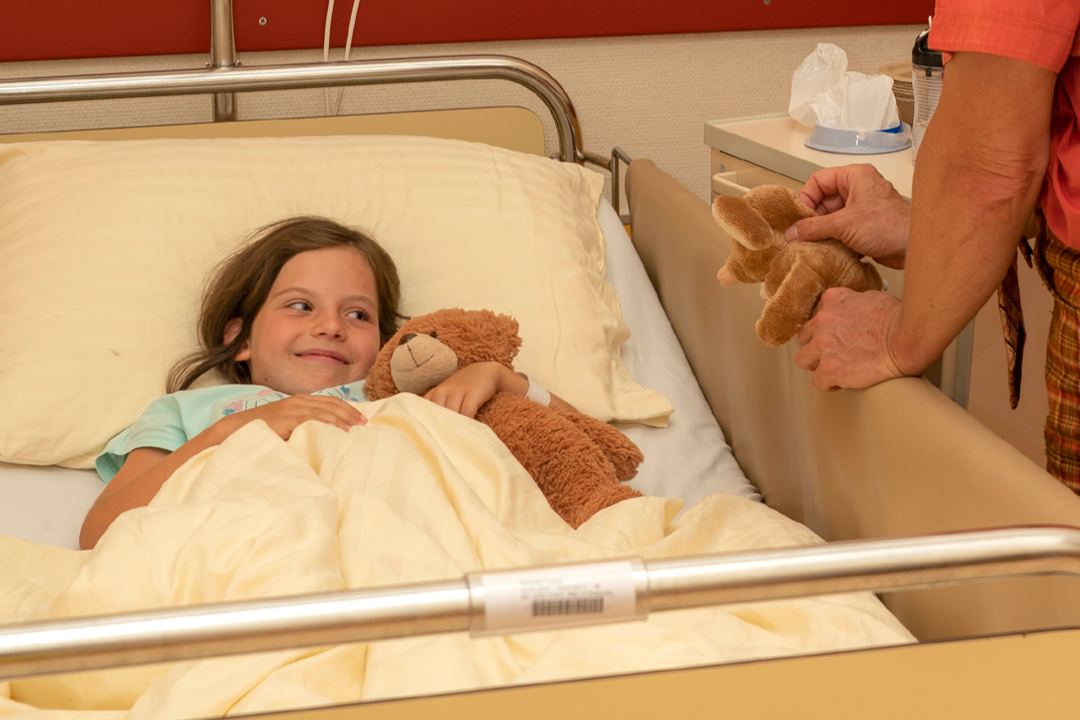 Laura liegt im Krankenbett mit ihrem Teddy und Mausi